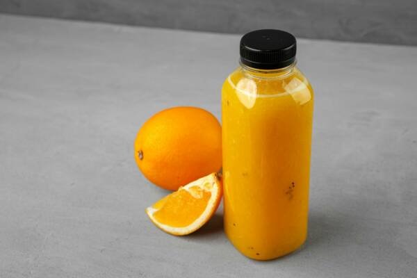 Bottle of freshly squeezed orange juice on gray background